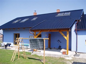 Modrý rodinný dům s tmavou taškovou střechou a dřevěným přístřeškem Modrý rodinný dům s tmavou taškovou střechou a dřevěným přístřeškem
